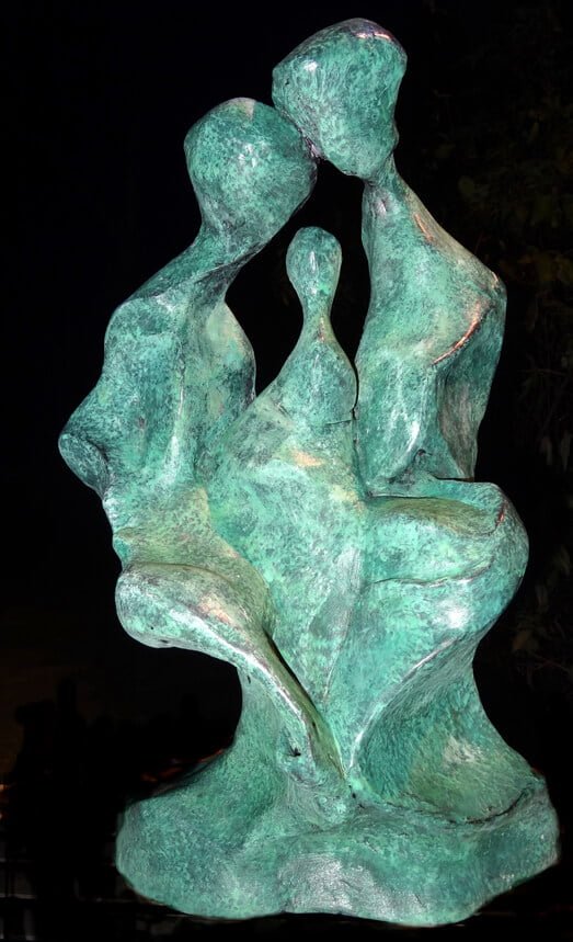 Tête-de-famille Tête-de-famille. This is a resin cast with the first verdigris patination colour. The photo shows the left side of a head, and the outline of an eyebrow, an eye, the nose, lips and chin are clear. The top of the head is formed by three figures implying father, mother and child.