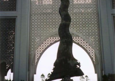 Bronze dagger sculpture with ceremonial arch behind, all flags flying for grand ceremonial. View away from stadium down pool.