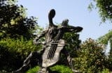 Tortelier - Bronze Sculpture of the cellist in the garden in bright sun. The sun is reflecting off the front of the bronze cello.