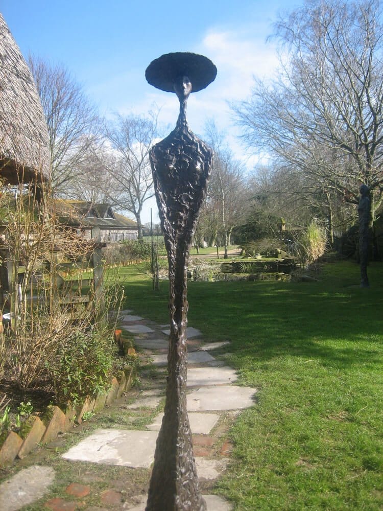 Sybil Sybil - a tall standing female figure, very slim with a wasp waist and arms parallel to her body wearing a wide-brimmed hat